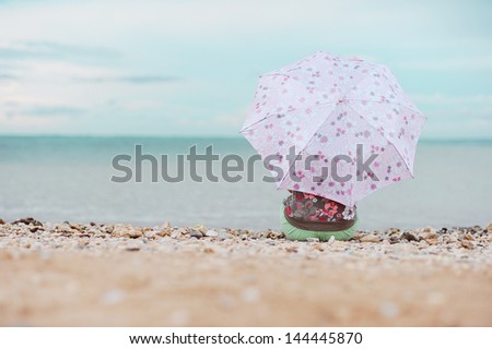 Girl sitting with umbrella at the sea shore in front of the sea alone outdoors