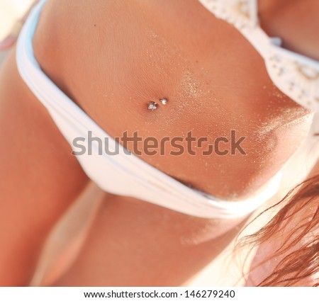 Beautiful sun tanned woman belly with piercing and swimsuit  at the beach