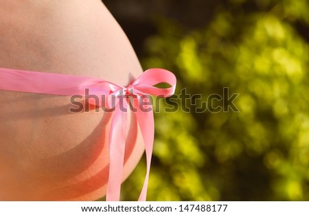 Pregnant woman tummy with pink ribbon and bow outdoors