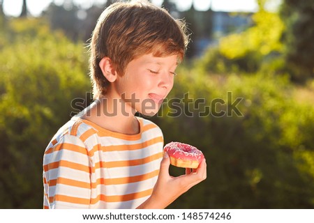 Young smiling teenager boy eating donut  outdoors, green background, doing bite