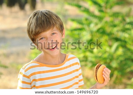Happy teenager boy eating hamburger outdoors