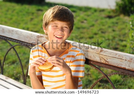 Happy smiling boy eating hamburger in park outdoors