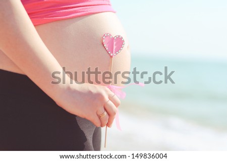 Pregnant woman tummy with pink cute heart outdoors at sea background