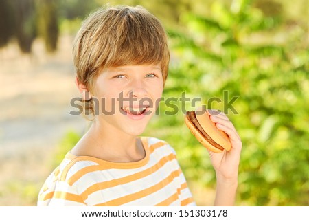Happy young teenager boy eating hamburger outdoors