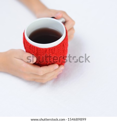Children hands holding red cup with knitted thing on it