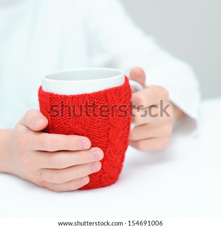 Child holding red cup with knitted thing indoors