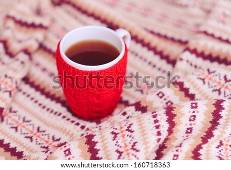 Red knitted cup with tea staying on knitted cover