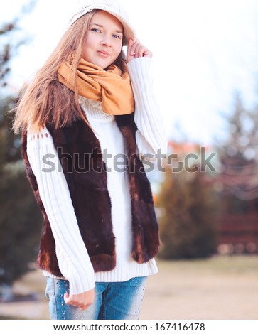 Stylish teenager girl in fur vest, white cap outdoors