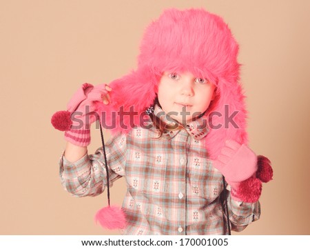 Young baby model in pink fur winter hat at beige background in studio