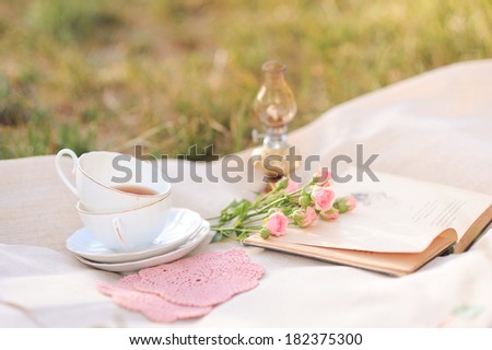 Cup of tea, open book, lamp, roses on cover outdoors