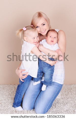 Young mother holding two children. Happy family over beige. Motherhood