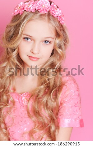 Smiling kid girl with long curly hair at pink background