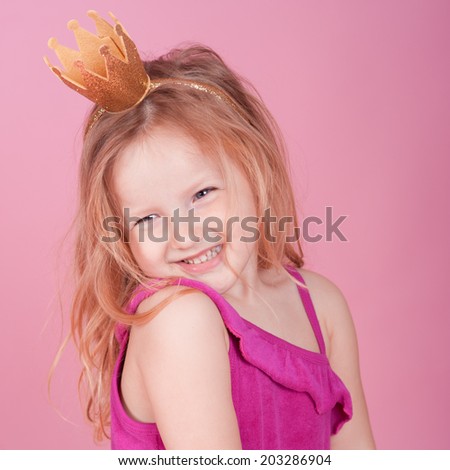 Laughing girl 3-5 years old wearing crown over pink