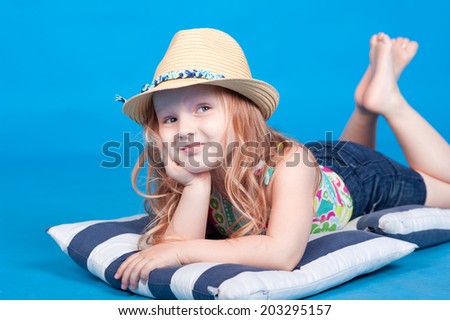 Cute kid girl 3-5 years old lying on striped pillows over blue. Marine theme