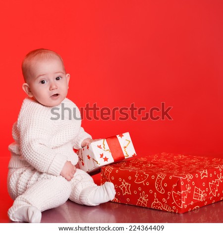 Portrait of baby wearing trendy knitted sweater, open christmas presents over red