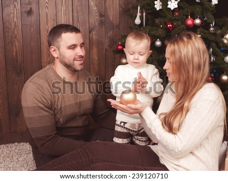 Stylish mother, father and their child celebrating christmas in room over christmas tree. Happy family. Wearing trendy knitted sweaters.