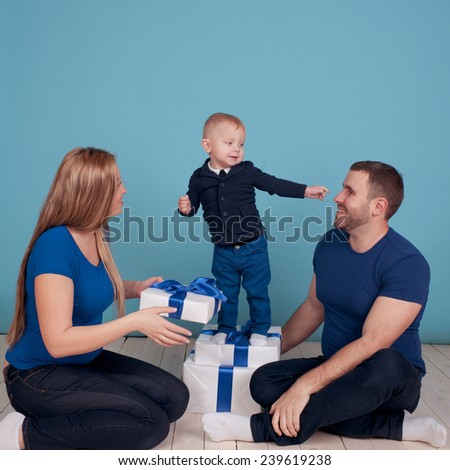 Happy family having fun in room over blue. Young blonde woman, man and their child unpacking christmas presents.