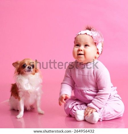 Funny cute baby girl playing with chihuahua over pink. Child laughing in room. Childhood.