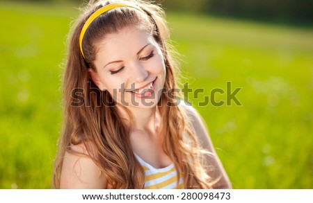 Smiling blonde girl 20-22 year old posing over green outdoors. Positive emotions. Young adults. Summer time.