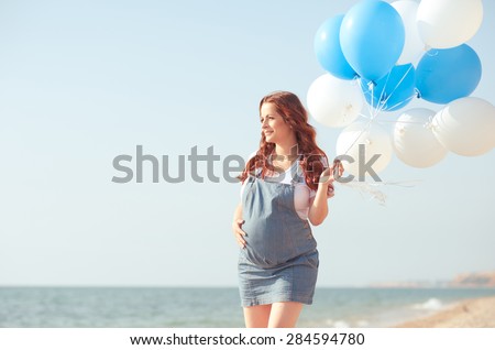 Pregnant woman holding air balloons outdoors. Walking at seashore. Motherhood. Maternity.