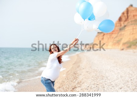 Happy pregnant woman playing with balloons outdoors. Resting at sea shore. Motherhood.