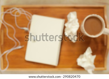 Blurred background of cup of coffee, notebook, crumpled paper, headphones on wooden tray. Working time.