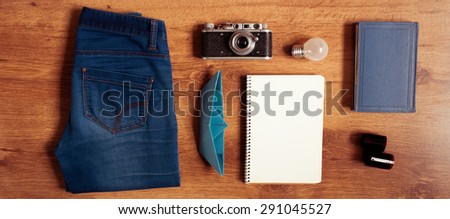 Vintage hipster packing: clothes, old camera, notebook,book,origami boat on wooden floor. Top view.