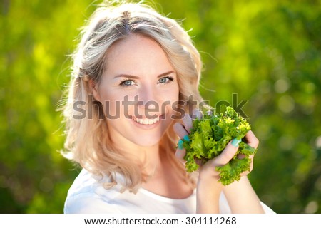Blonde woman 20-22 year old holding lettuce over nature background. Looking at camera smiling. Healthy lifestyle. Young adults.