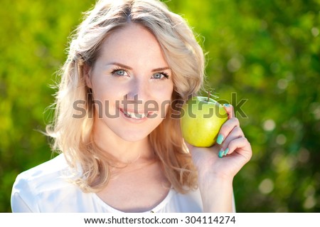 Smiling girl 20-24 year old holding green apple outdoors closeup. Looking at camera. Posing over green nature background. Healthy eating.