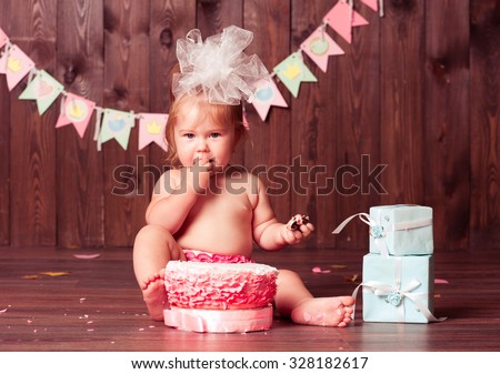 Baby girl 1 year old eating birthday cake in room. Birthday party. Looking at camera. Childhood.