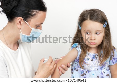 female doctor pediatrician with breathing mask over mouth giving child an intramuscular injection in arm