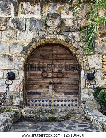 vintage wooden gate with two iron door handle knockers and big locker build in stone wall; rhinos head with chains as handrail on both sides