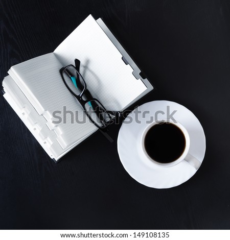 Open Book with glasses and a cup of coffee on black office table. Top view