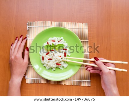 Woman is eating rice with berries, holding chopsticks. top view