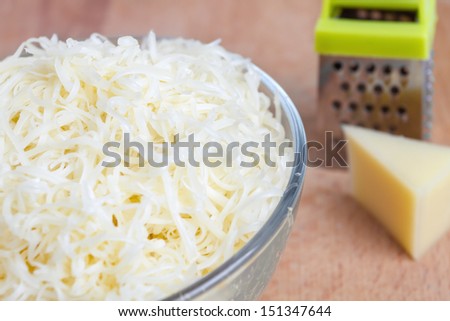Grated cheese in a bowl, grater, a piece of cheese on a wooden table
