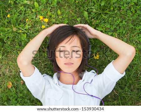 Young woman enjoying the music with closed eyes on a summer meadow