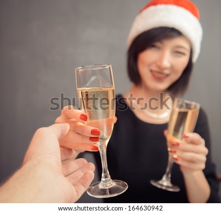 Young woman in santa hat is giving glass with champagne