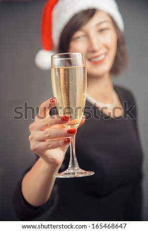 Happy woman in santa hat is giving tumbler with champagne on a gray background