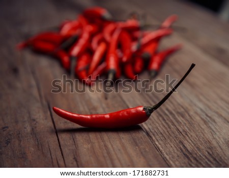 One chili pepper is separate from the pile of peppers on a wooden table