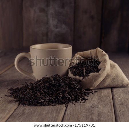 Cup of black tea next to a black leaf tea on a wooden table