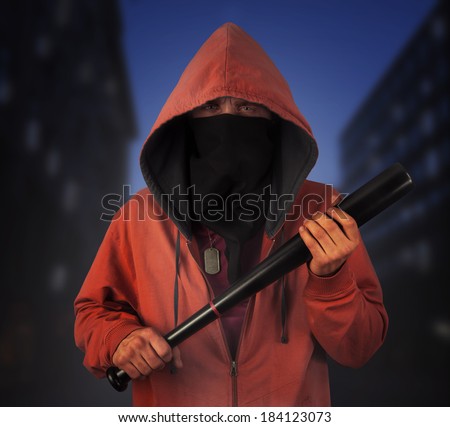 Angry hooligan in the mask holds baseball bat on the background of night city