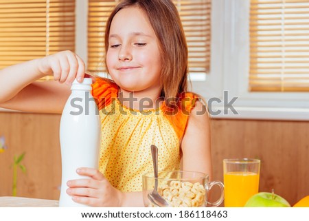 Little girl opens bottle of milk for cereal flakes