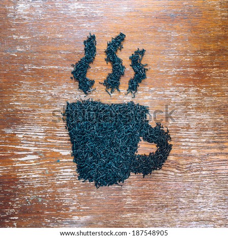Black leaf tea in the shape of cup on a wooden table
