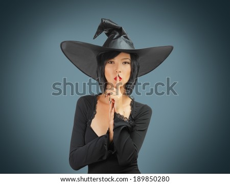 Beautiful Halloween witch makes silence gesture on a gray background