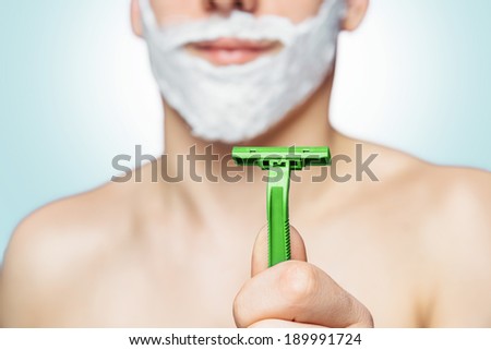 Man with foam on his face holds green razor