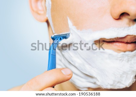 Man with foam on his face is shaving with razor, close-up