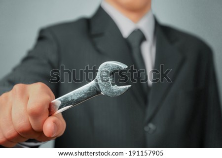 Businessman in a suit holds wrench, focus on wrench, concept of business creation