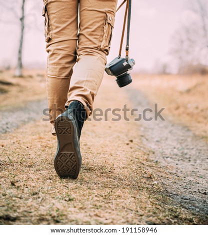 Traveler woman with old photo camera walks on a road, face is not visible