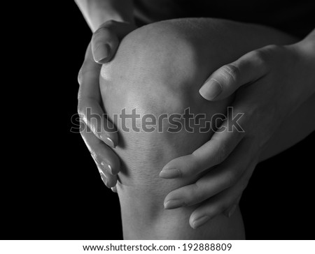 Woman holds her knee, pain in the knee joint, monochrome image