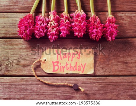 Red hyacinths and greeting card with text Happy Birthday on a wooden table